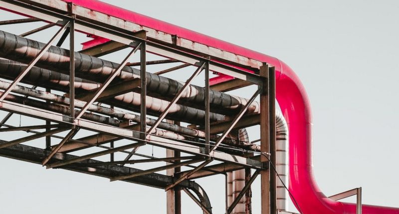 A pipeline, owner unknown, runs across the screen. A grey scaffolding structure holds up a newer added pipe in pink.