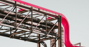 A pipeline, owner unknown, runs across the screen. A grey scaffolding structure holds up a newer added pipe in pink.