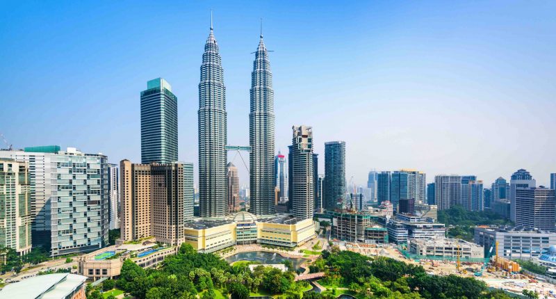 An image of the capital city of Malaysia taken from a distance with two large towers identical in height standing in front of a green park space