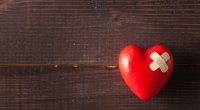 Red broken heart with a band-aid on a wooden background