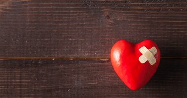 Red broken heart with a band-aid on a wooden background