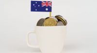 The flag of Australia sticks out of a cup of coins.