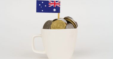 The flag of Australia sticks out of a cup of coins.