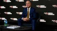 Chris Ellison sits in front of several Mineral Resources logos.