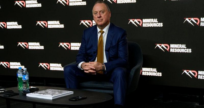 Chris Ellison sits in front of several Mineral Resources logos.