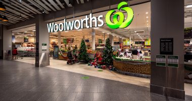 A Woolworths logo hangs over a supermarket entrance.