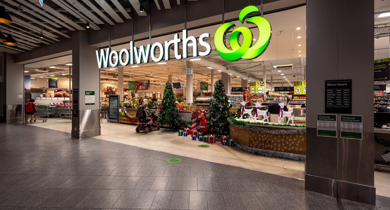 A Woolworths logo hangs over a supermarket entrance.