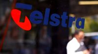 A Telstra logo on the side of a window. You can see a man on his phone in the background.