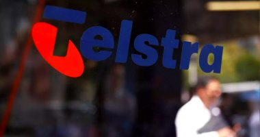 A Telstra logo on the side of a window. You can see a man on his phone in the background.