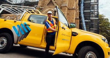 A man getting out of a Johns Lyng Group-branded yellow truck.