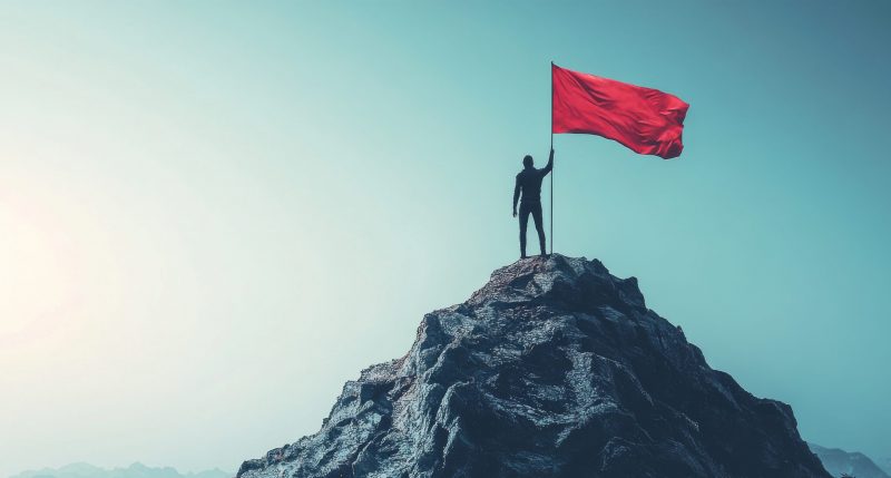 Person hoisting a red flag on a mountain