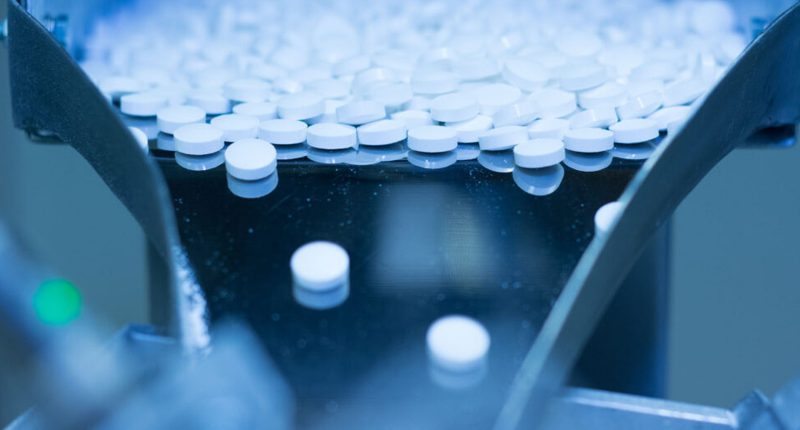 White pills pouring down a shoot at the AFT Pharmaceuticals company labratory.