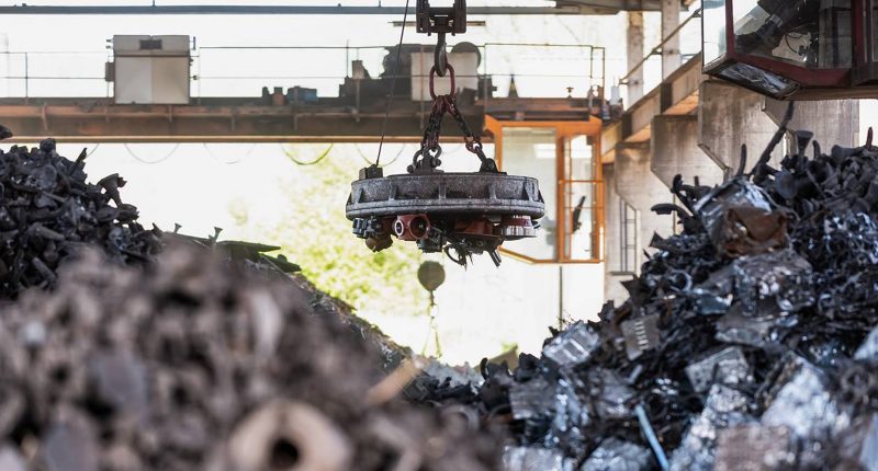 An e-waste machine hangs over piles of garbage.