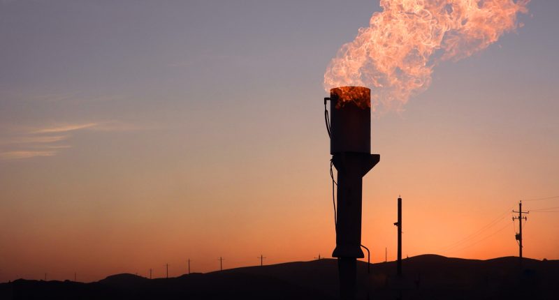 A gas nozzle spits out fire against a sunset.