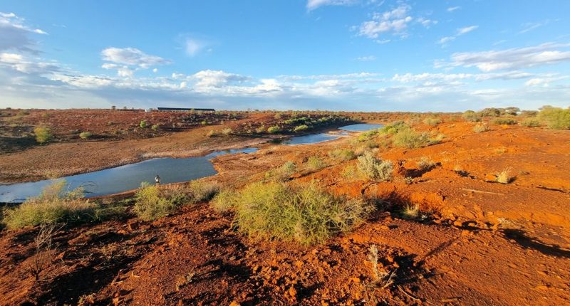 A dusty red dirt embankment alongside a small blue river.