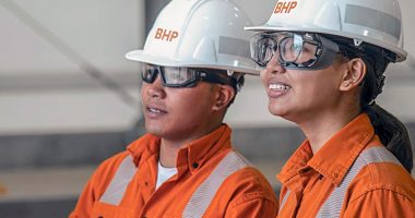 Two BHP Group workers in safety gear wearing hard hats.