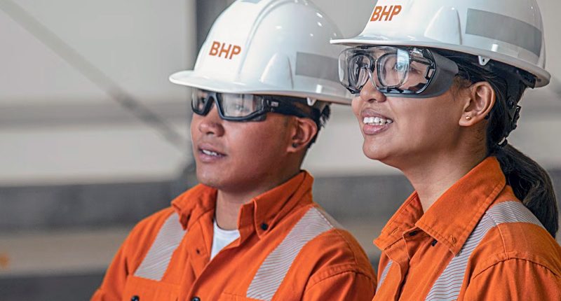 Two BHP Group workers in safety gear wearing hard hats.