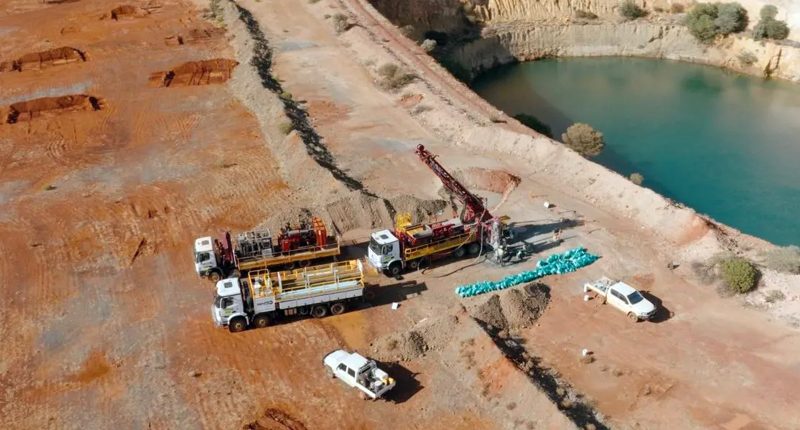 Several Brighstar trucks parked near a dirt barricade on the edge of a deep mining pool.