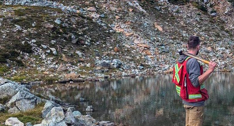 An Equinox Resources worker with safety gear on carrying a hammer while standing over a rock pool.