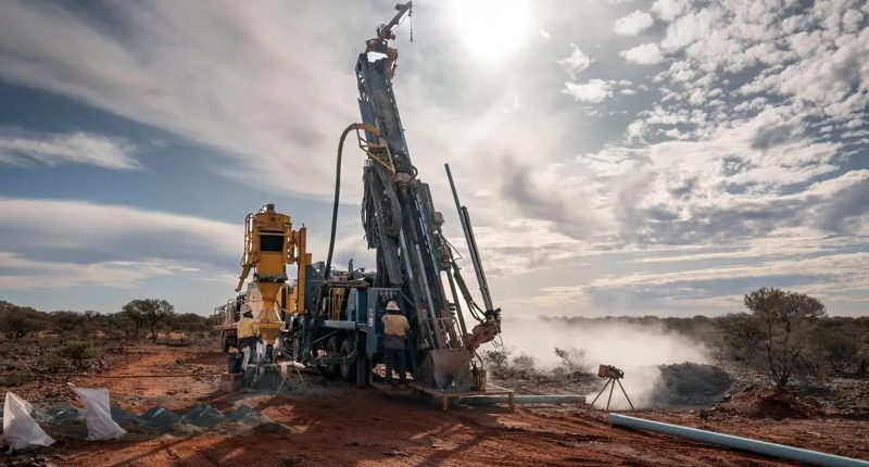 A large mining rig surrounded by dust kicked up from the brown earth at its base.