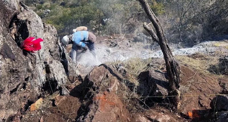 A Golden Deeps explorer works on a rocky cliff. Safety tape is wrapped around several rocks.