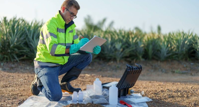 A Victory Metals employee in safety gear checks over test results on a rock plain.