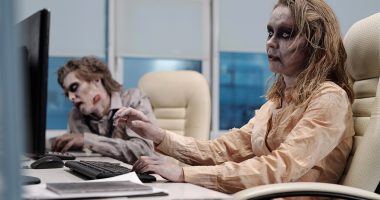 Two zombie works sit at an office desk.