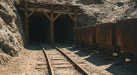 A rustic and aesthetic view of an abandoned mine entrance with weathered wooden beams, railroad tracks, and old rusty ore carts