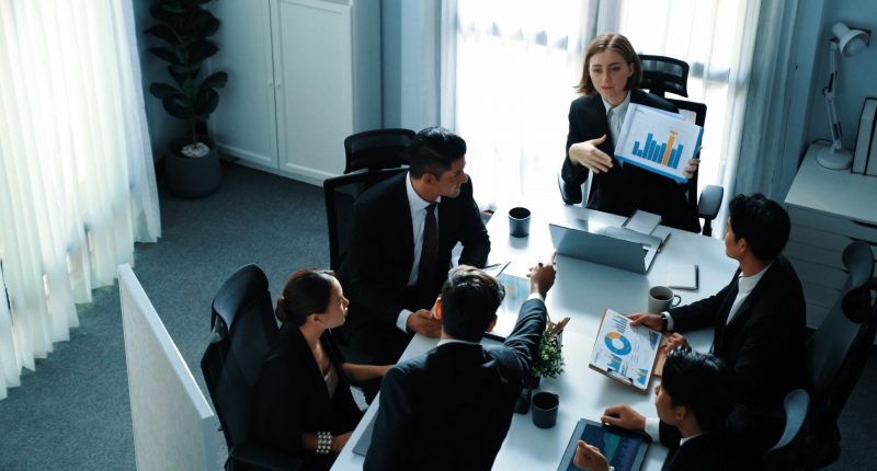 Top view of skilled project manager holds increasing stock market investment chart while businessman explains idea and present marketing strategy at meeting room. Team working together.