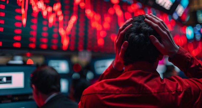 Wall Street investors, hands on head, gaze upward at red charts on crowded trading floor, conveying despair.