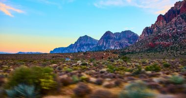Experience the tranquil beauty of Red Rock Canyon at sunset near Las Vegas. Rugged red and gray mountains with desert vegetation create a dramatic and serene scene in the heart of Nevada.
