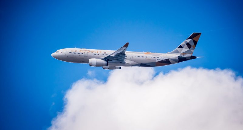 BRUSSELS, BELGIUM. 11th July 2018. Etihad Airways Airbus A330 in flight: A long distance shot of an Etihad Airways passenger airplane flying through a blue sky with soft white clouds. The aircraft features the Facets of Abu Dhabi livery.